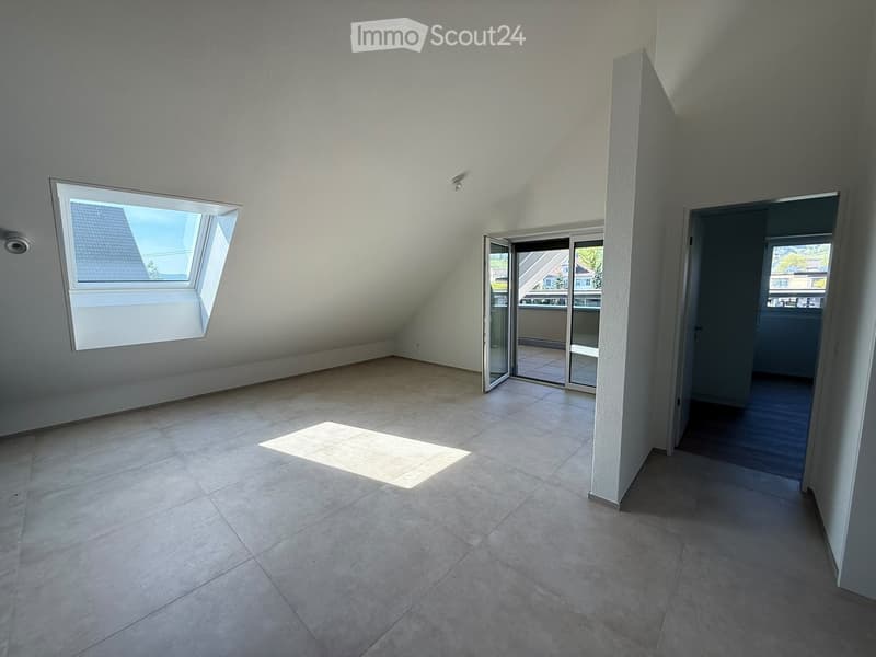 Empty attic room with tiled floor, skylight window, and sliding glass door leading to a balcony.