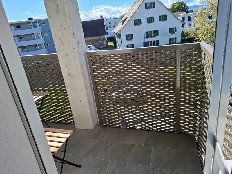 Balcony with a decorative metal gate, tiled floor, and a small wooden bench visible in the background.
