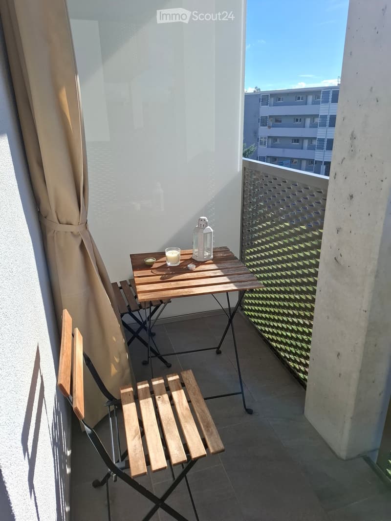 Balcony with wooden table, chairs, lantern, and cup, overlooking a building.