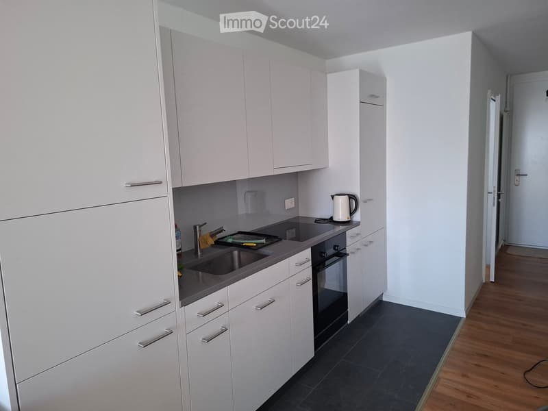 Modern kitchen with white cabinets, stainless steel sink, oven, and electric kettle on the counter.