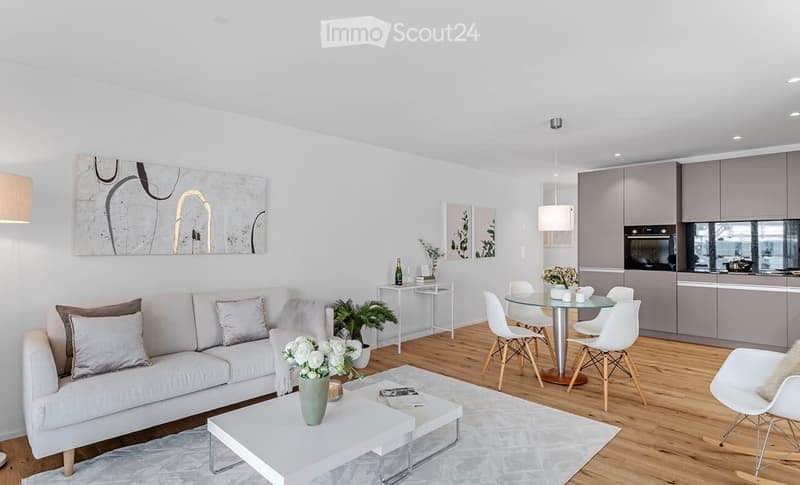 Modern, open-concept living and dining area with a white sofa, coffee table, dining table with chairs, kitchen area with cabinets and appliances, and decorative artwork on the walls.