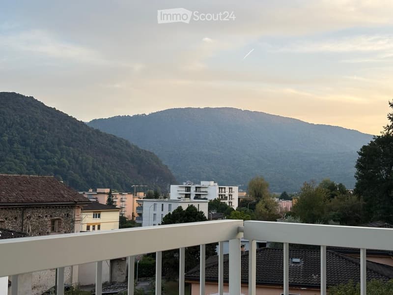 Balcony with white railing overlooking a cityscape and mountains in the background.