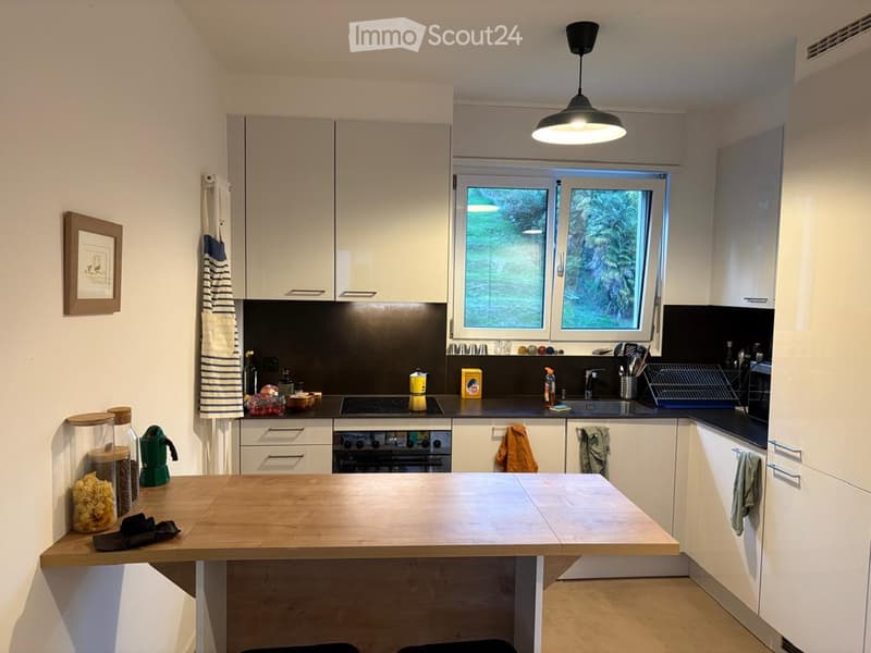 Modern kitchen with white cabinets, a central island, and various appliances including an oven, blender, and cups on the counter.
