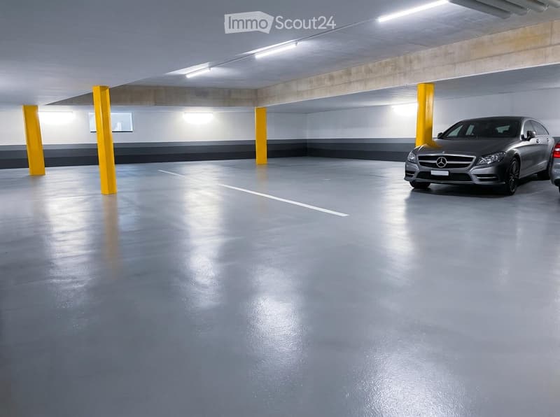Underground parking area with a single car parked, concrete pillars, and fluorescent lighting.