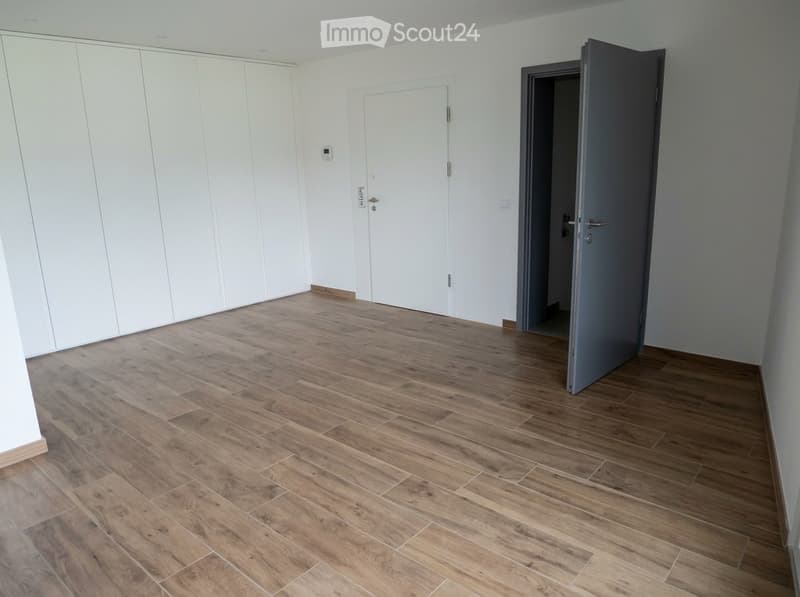 Empty room with wooden flooring, white walls, and built-in white wardrobes. Two doors are visible, one leading to another room.