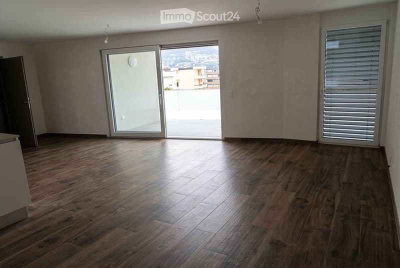 Empty room with wooden flooring, large sliding glass door leading to a balcony with a city view, and a window with blinds.
