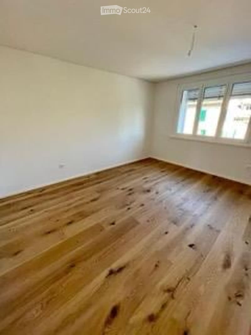 Completely empty room with wooden flooring and large windows, no furniture or equipment.