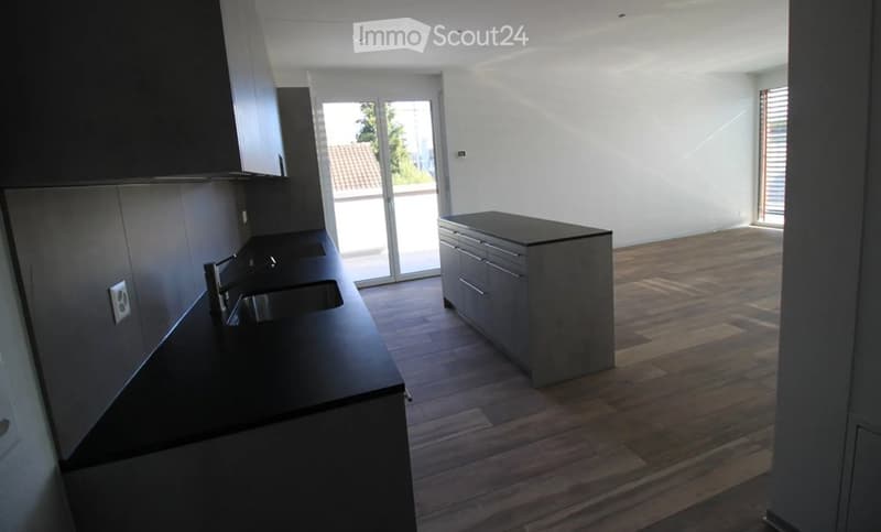 Modern, unfurnished kitchen with dark countertops, built-in cabinets, and a central island. Large sliding glass door leads to a balcony.