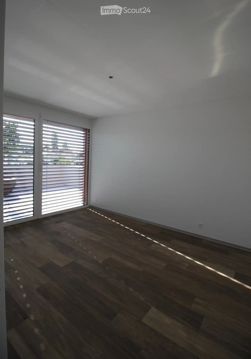 Empty room with wooden flooring and large windows with blinds, allowing natural light to fill the space.