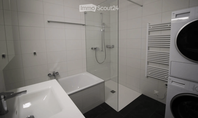 Modern bathroom with white tiled walls, a bathtub, a glass-enclosed shower, a sink, a radiator, and a washing machine.