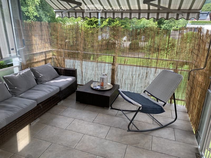 Balcony with a wicker sofa, a wicker chair, a small table with a lantern, and a bamboo privacy screen.