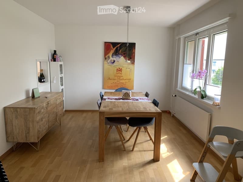 Bright dining area with wooden floor, large window, dining table with chairs, cabinet, and decorative items.