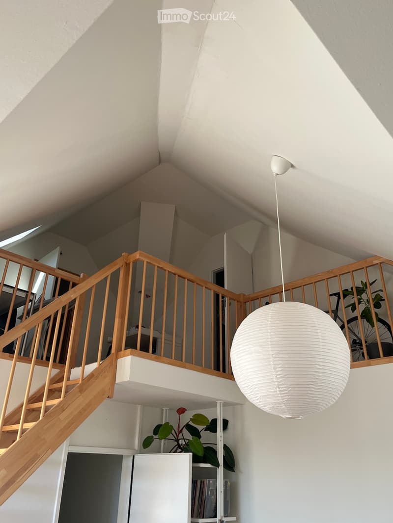 Open staircase with wooden railings and a hanging spherical light fixture, leading to an upper level with visible plants and a bicycle in the background.