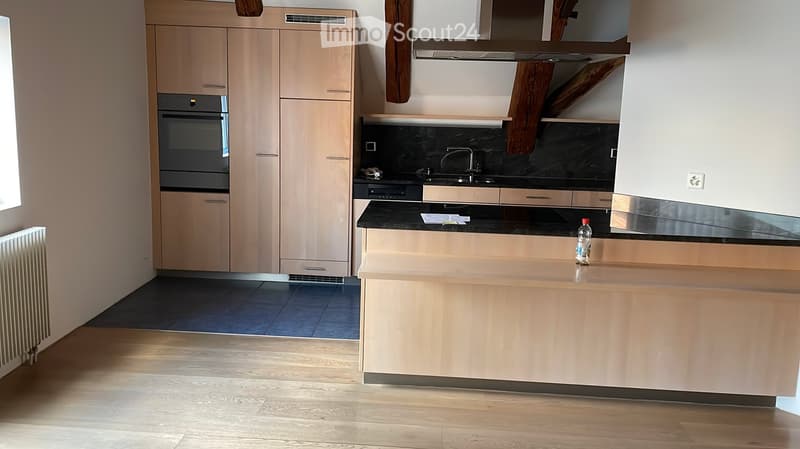 Modern kitchen with light wood cabinets, black countertops, stainless steel appliances, and a central island.