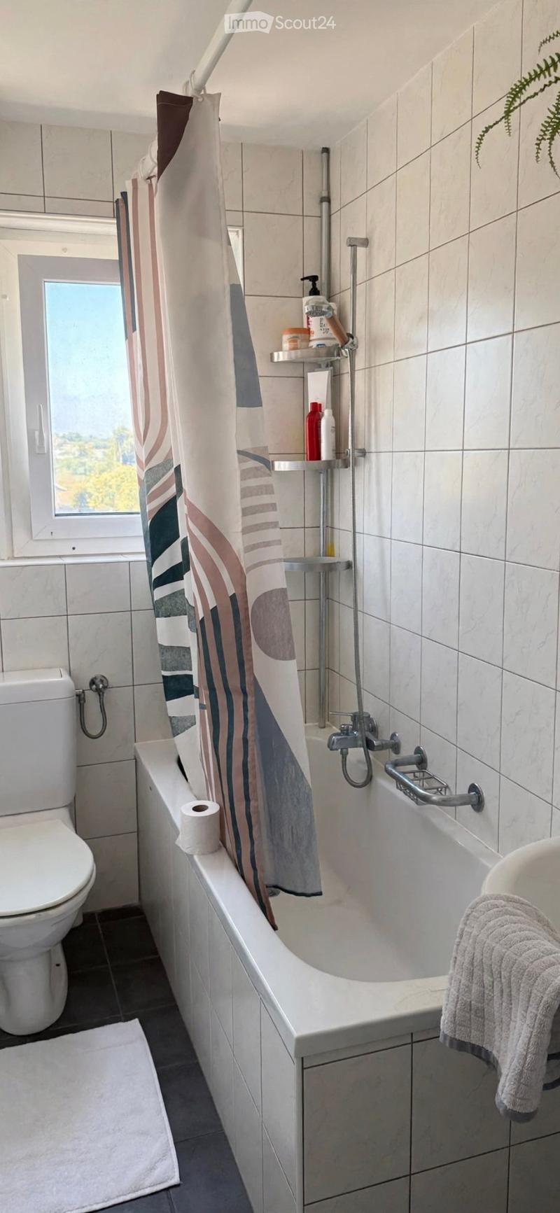 Modern bathroom with a bathtub, toilet, shower curtain, towel, toilet paper, and a shower shelf with bottles.