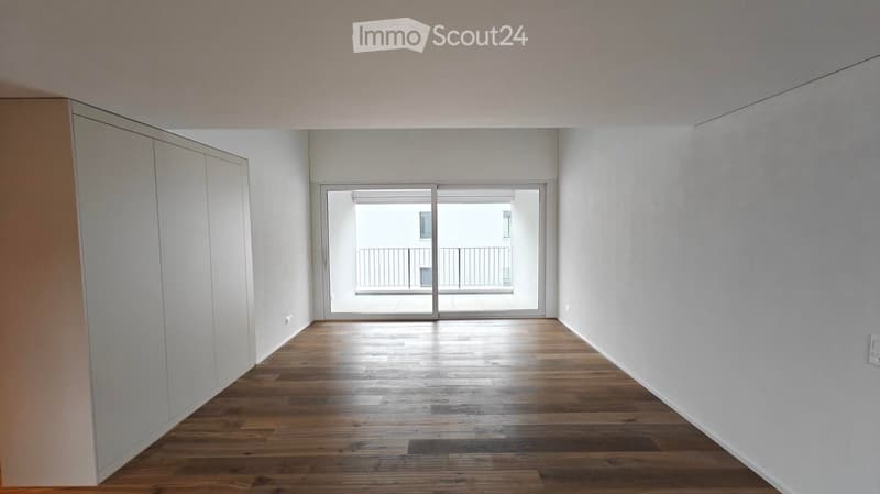 Empty room with wooden flooring, white walls, and a sliding glass door leading to a balcony.