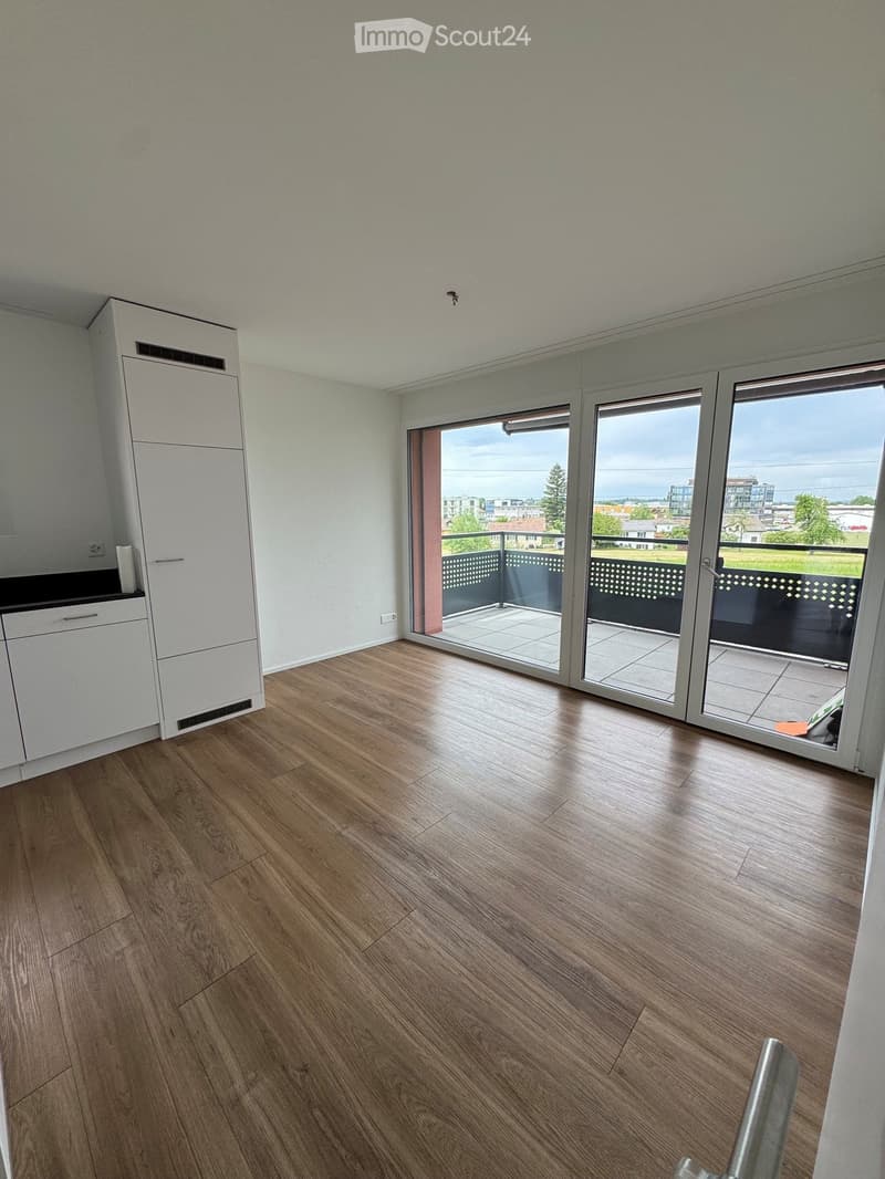 Empty room with wooden flooring, white cabinetry, and large sliding glass doors leading to a balcony with a view of the landscape.