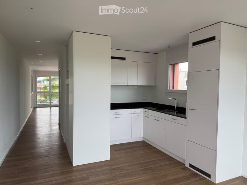 Modern hallway with white cabinetry, wooden flooring, and a small kitchen area visible at the end.