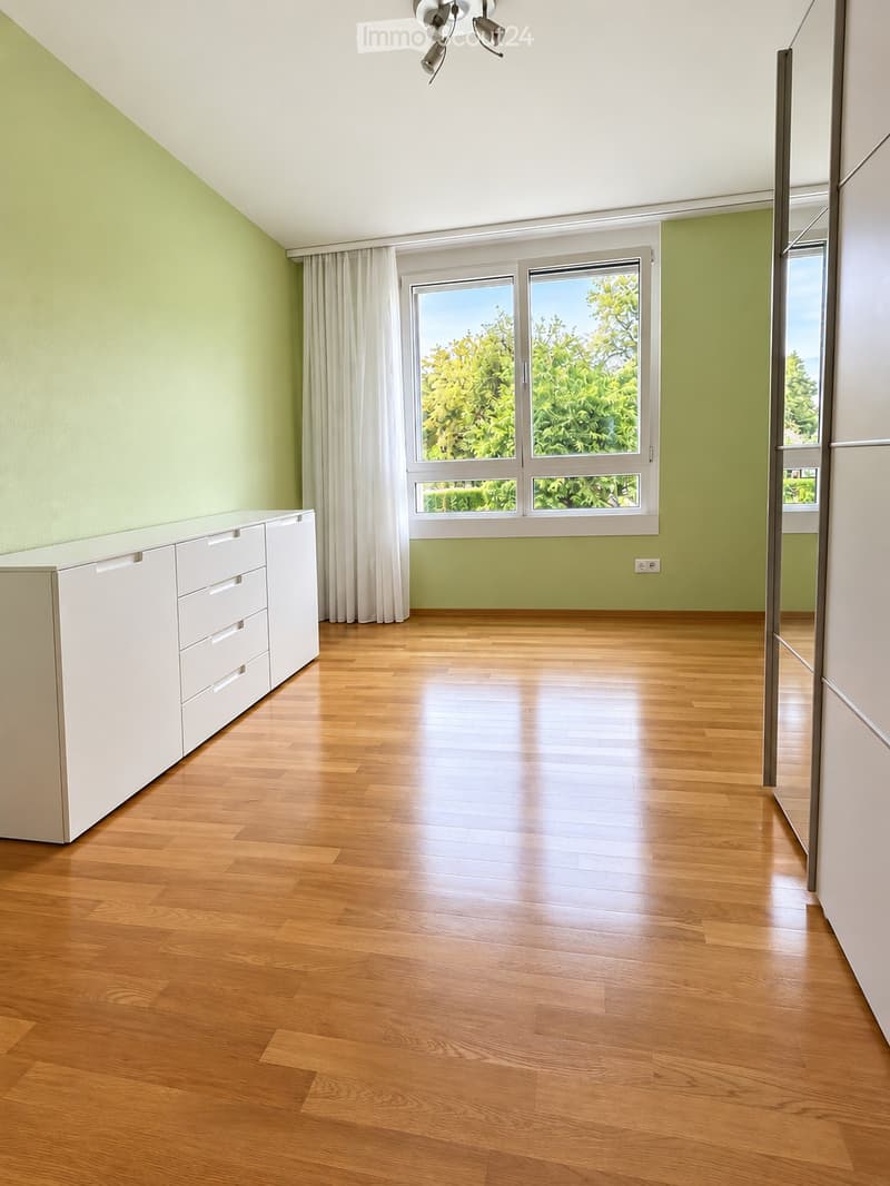 Empty room with wooden flooring, white cabinet, large windows with curtains, and a ceiling light fixture.