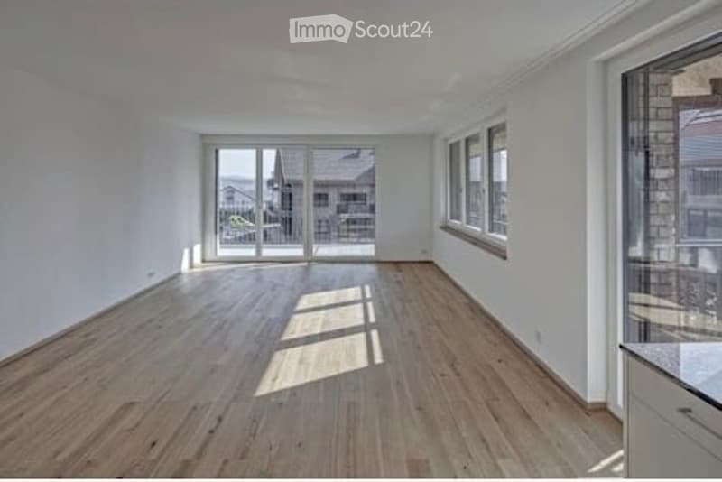 Bright, empty room with wooden flooring, large windows, and sliding glass doors leading to an outdoor area.