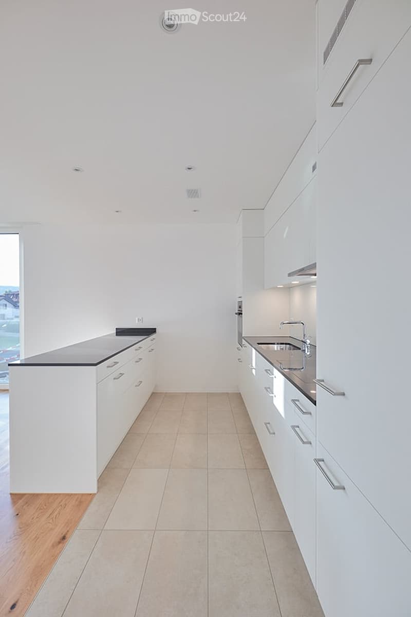 Modern, minimalist kitchen with white cabinets, black countertops, and a stainless steel sink. The space features light-colored tiles and a wooden accent wall.