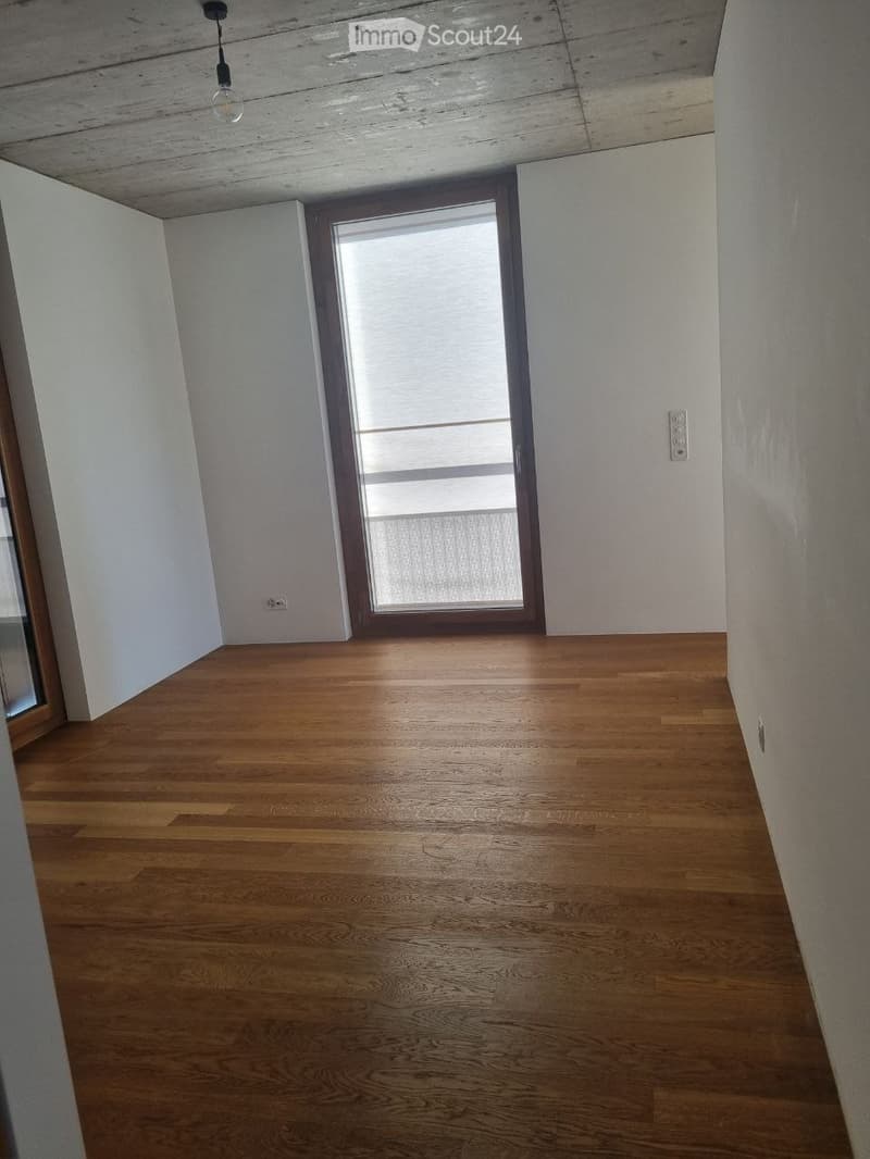 Empty room with wooden flooring, white walls, and a large window with blinds. No furniture or equipment is present.