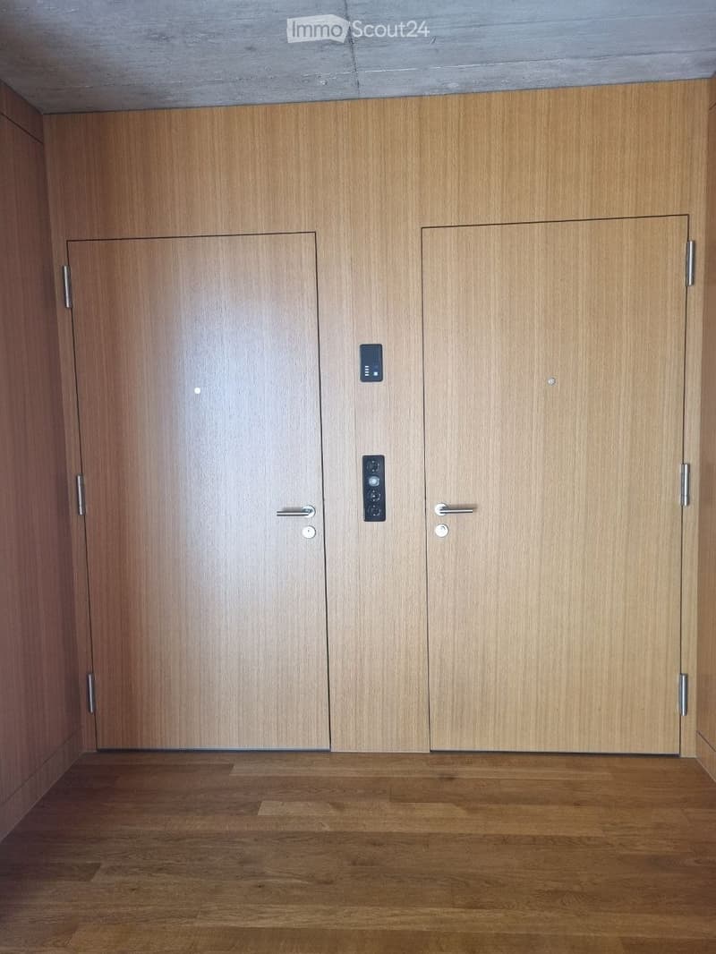 Empty hallway with wooden doors and a polished wooden floor, featuring modern door handles and a small control panel.