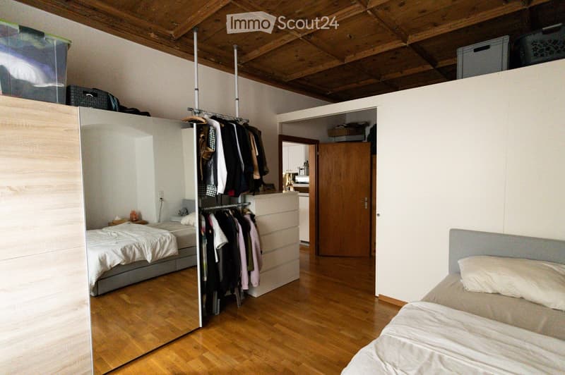 Spacious bedroom with wooden flooring, two single beds, large mirrored wardrobe, and clothing rack. The room features a wooden ceiling and a doorway leading to another room.