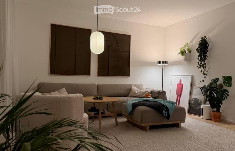 Modern living room with a grey sectional sofa, wooden coffee table, ottoman, floor lamp, and decorative art pieces.