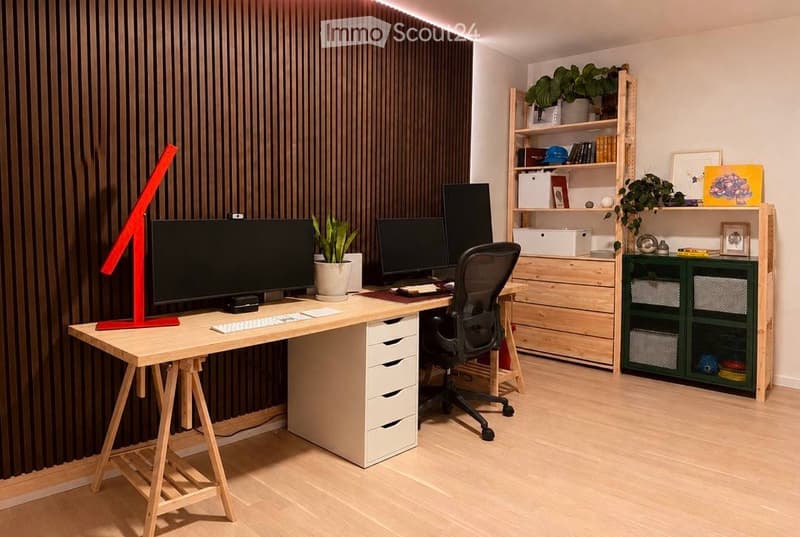 A modern, well-organized home office with a large wooden desk, multiple computer monitors, a comfortable office chair, and a variety of storage solutions including shelves and cabinets. The room features a sleek design with a combination of natural wood a
