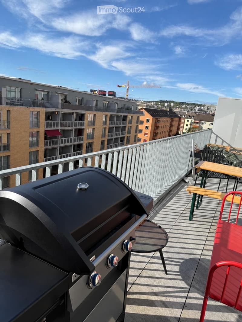 Balcony with a grill, table, and chairs, overlooking a cityscape with modern buildings and a clear blue sky.