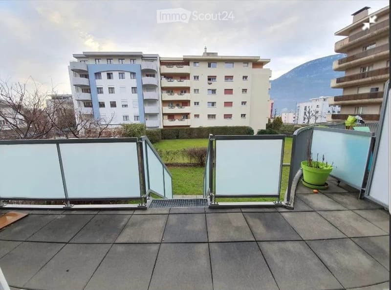 Balcony with grey tiled floor, glass balustrade, and a green potted plant on the right side.