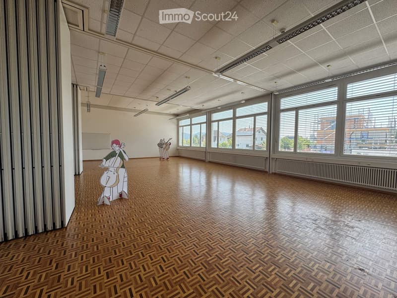 Empty room with wooden herringbone flooring, large windows with blinds, and a whiteboard on the wall. No furniture or equipment present.