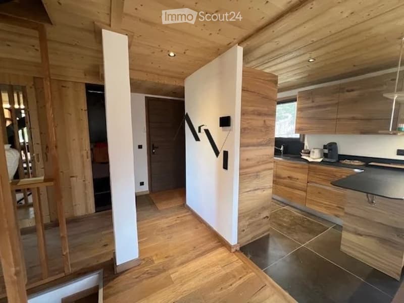 Modern, minimalist kitchen with wooden cabinetry, a sleek black countertop, and a stainless steel sink. The space features warm wooden flooring and wall paneling, creating a cozy yet contemporary atmosphere.
