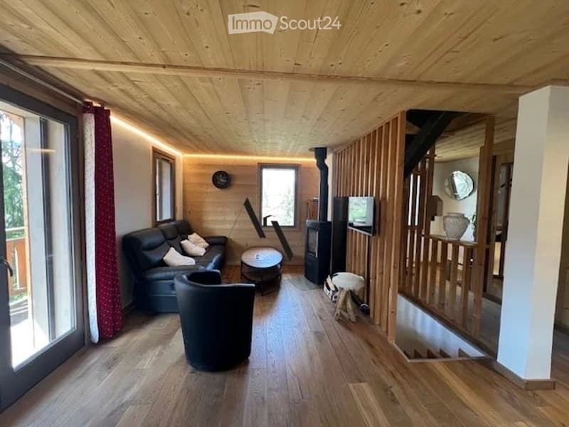 Cozy living room with wooden ceiling and floor, large windows, fireplace, sofa, coffee table, and decorative items.