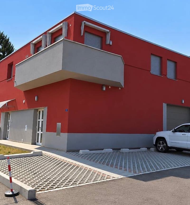 Two-story house with red brick exterior, white trim, balcony on the second floor, garage, and a paved driveway.