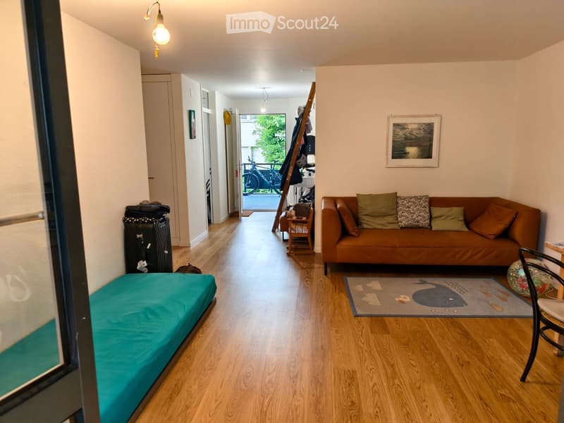 A furnished room with a sofa, pillows, a chair, a small table, a picture frame, a suitcase, and a bed with a blue cover.