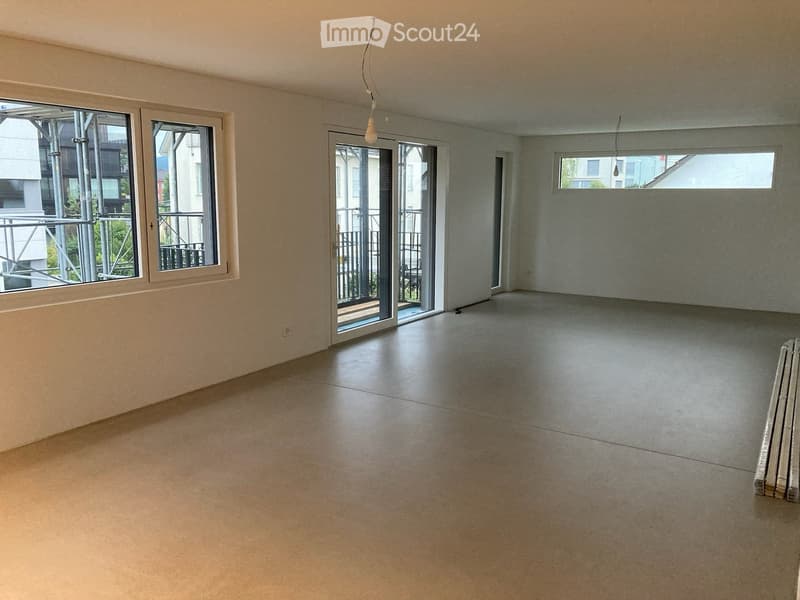 Empty room with smooth concrete floor, large windows, and sliding glass doors leading to a balcony.