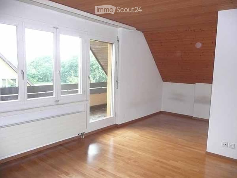 Empty attic room with wooden floor, white walls, large windows, and a sliding glass door leading to a balcony.