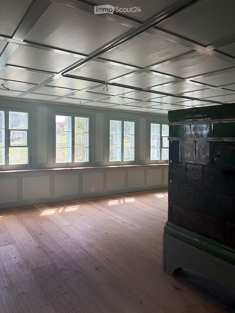 Empty room with wooden flooring, large windows, and a slanted ceiling with skylights.
