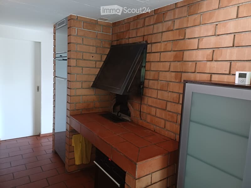 Brick-walled kitchen with a wooden countertop, built-in oven, and refrigerator. A yellow jacket is hanging on the wall.