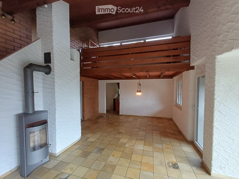 Empty hallway with tiled floor, exposed wooden ceiling beams, and a modern wood-burning stove on the left side.