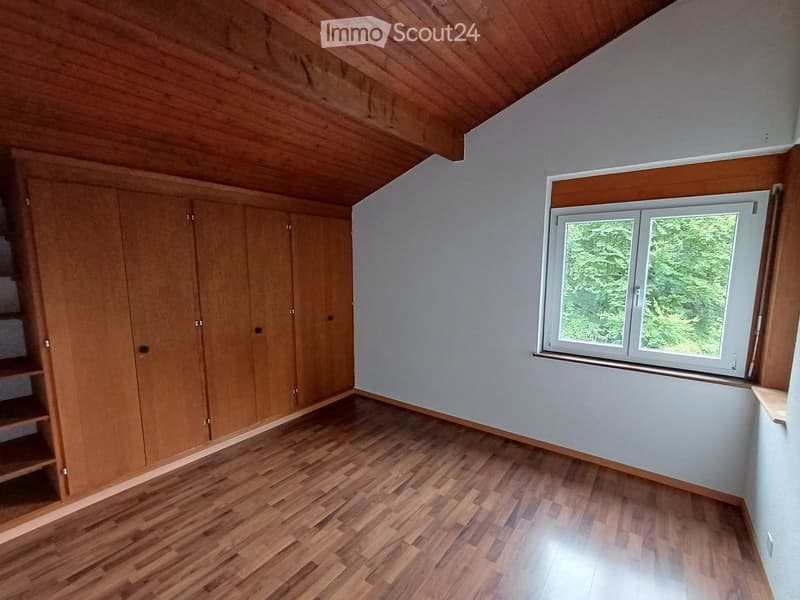 Empty room with wooden flooring, wooden built-in wardrobes, and a large window showing greenery outside.