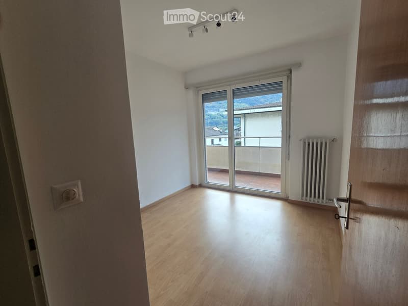 Empty room with wooden flooring, white walls, and a sliding glass door leading to a balcony with a view.