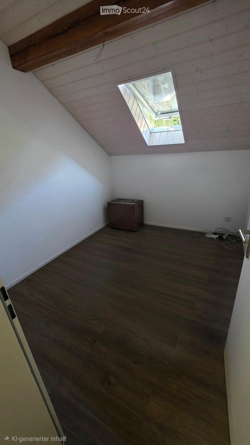 Empty attic room with wooden flooring, white walls, exposed wooden beams, and a skylight window.