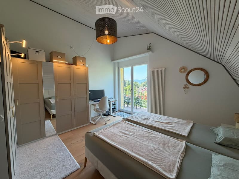 Cozy attic bedroom with two single beds, a desk with a computer, a wardrobe, and a large window offering a scenic view.