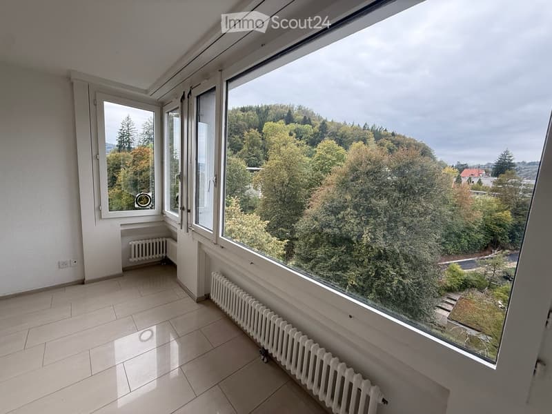 Empty room with tiled floor, large windows, radiators, and a view of trees and a house outside.