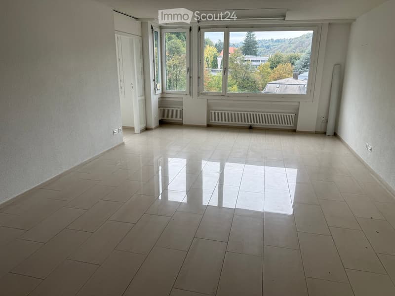 Empty room with tiled floor, large windows, radiators, and a door leading to another space.