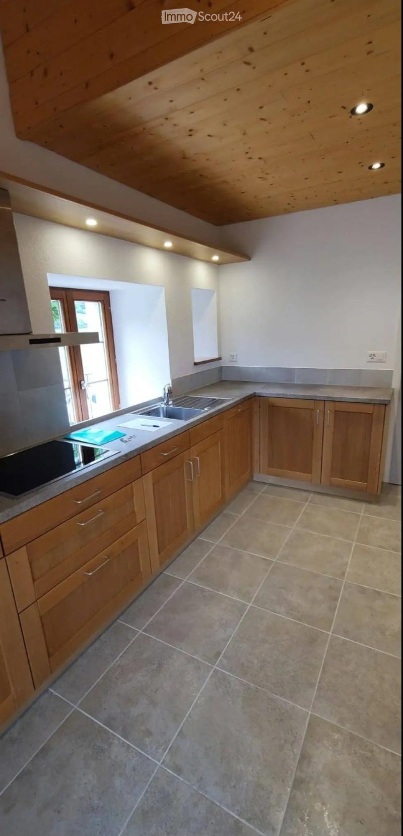 Modern kitchen with wooden cabinets, stainless steel sink, and tiled floor.