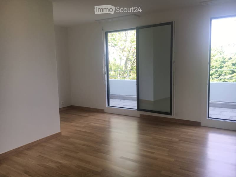 Empty room with wooden flooring, large sliding glass doors leading to a balcony, and white walls.